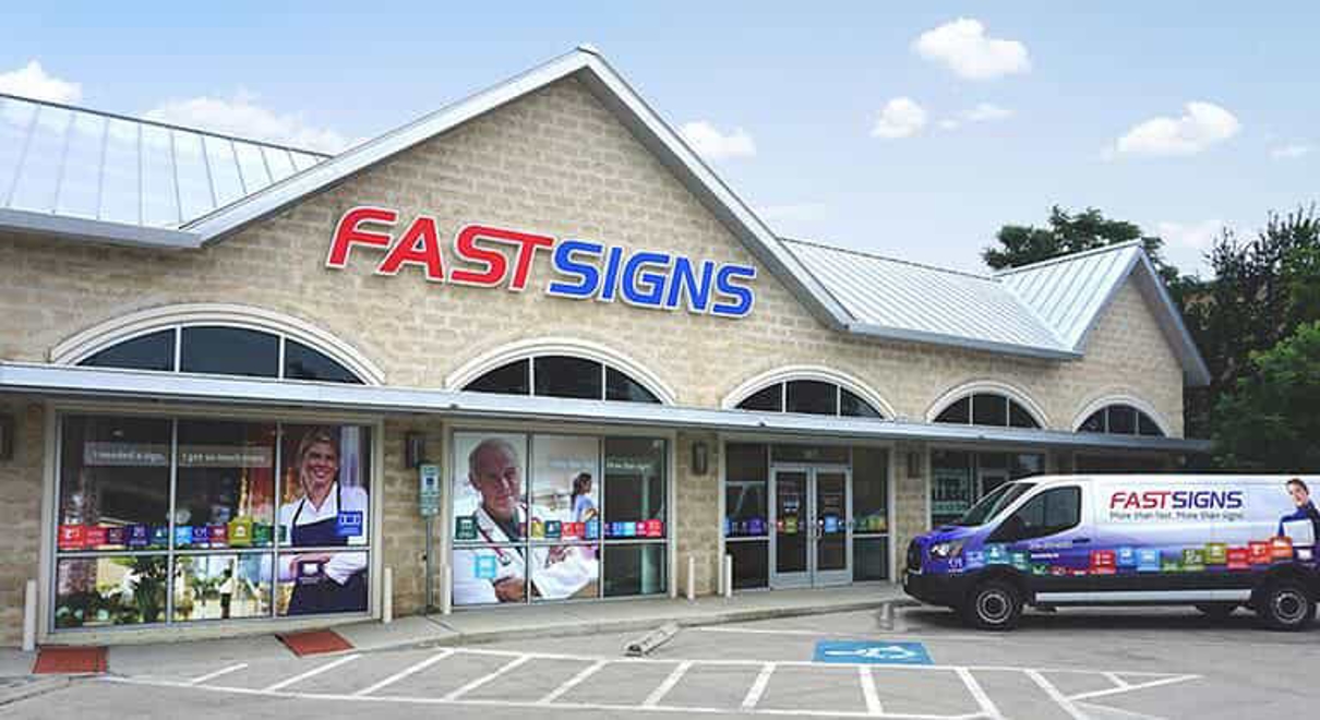 A FASTSIGNS van is parked outside of a FASTSIGNS building
